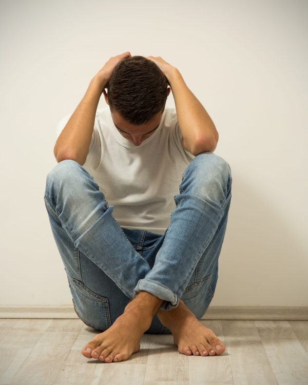 Young man sitting on a floor with hands on head. Vignette added